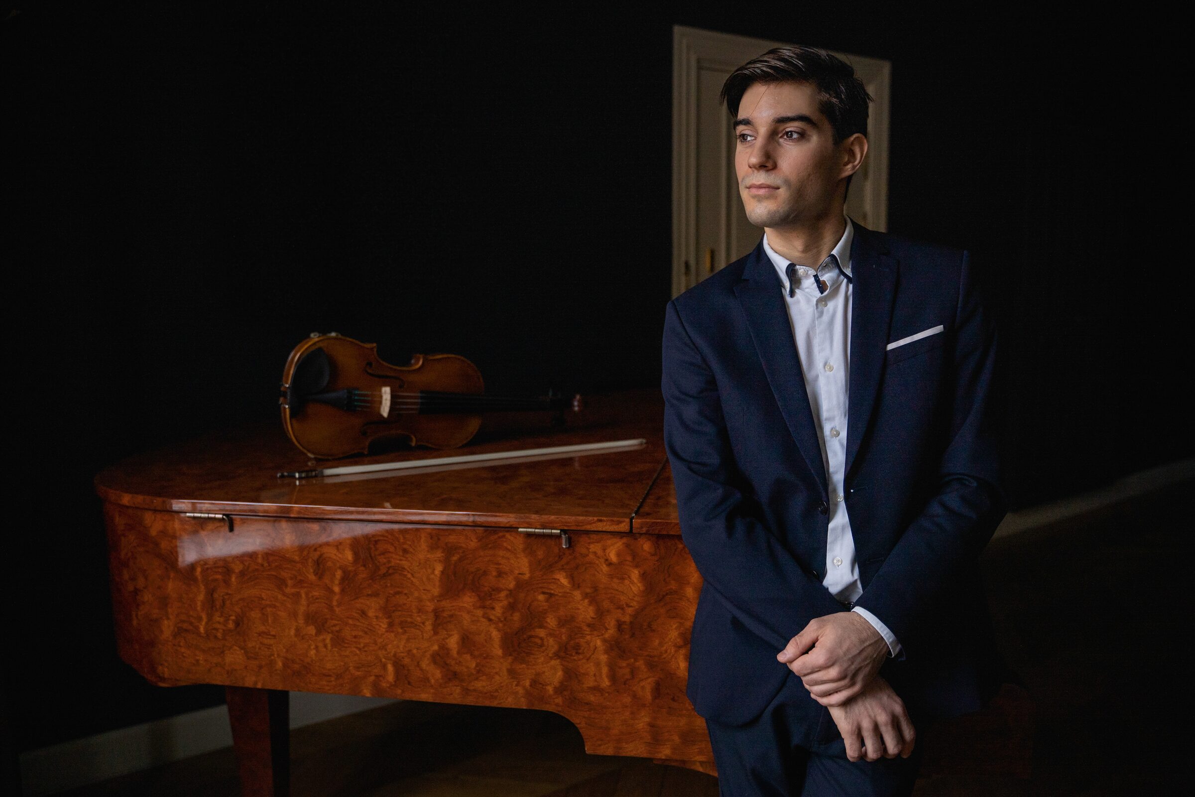 Alejandro Boix apoyado en un piano de cola con su violín
