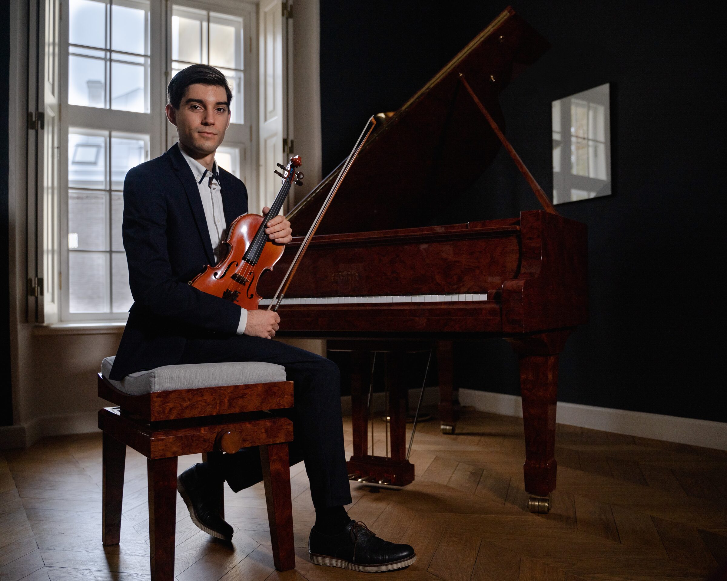 Alejandro Boix sentado junto a un piano de cola, sosteniendo su violín