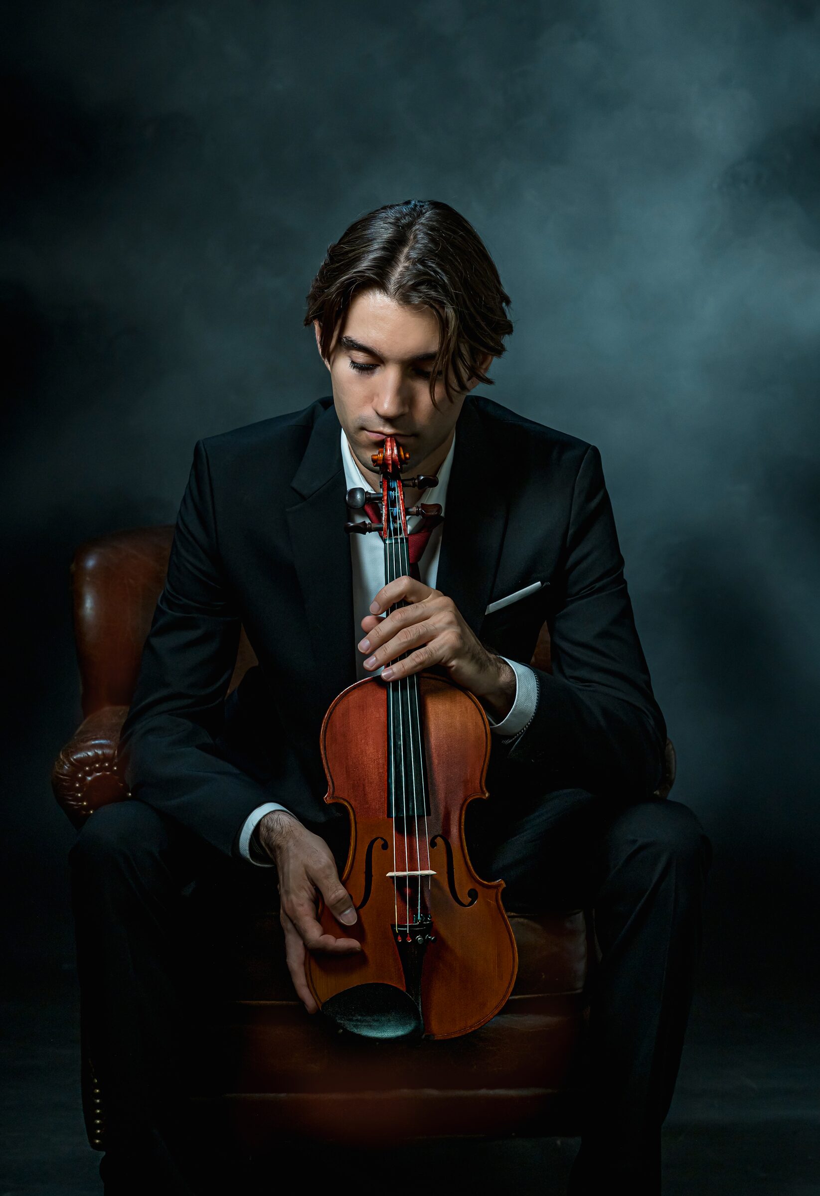 Alejandro Boix sentado con su violín, retrato de estudio en tono oscuro